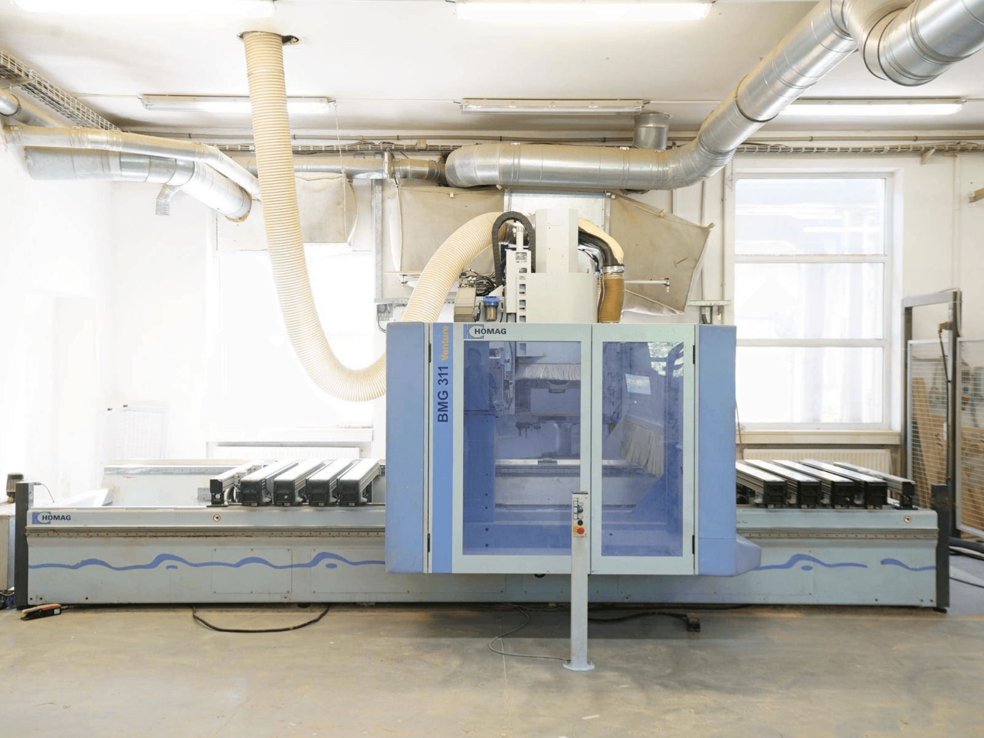 Centre d'usinage CNC pour le bois HOMAG V BMG 311/42/F/K, vue de face, doté d'une grande table de travail et d'un système d'aspiration des poussières.
