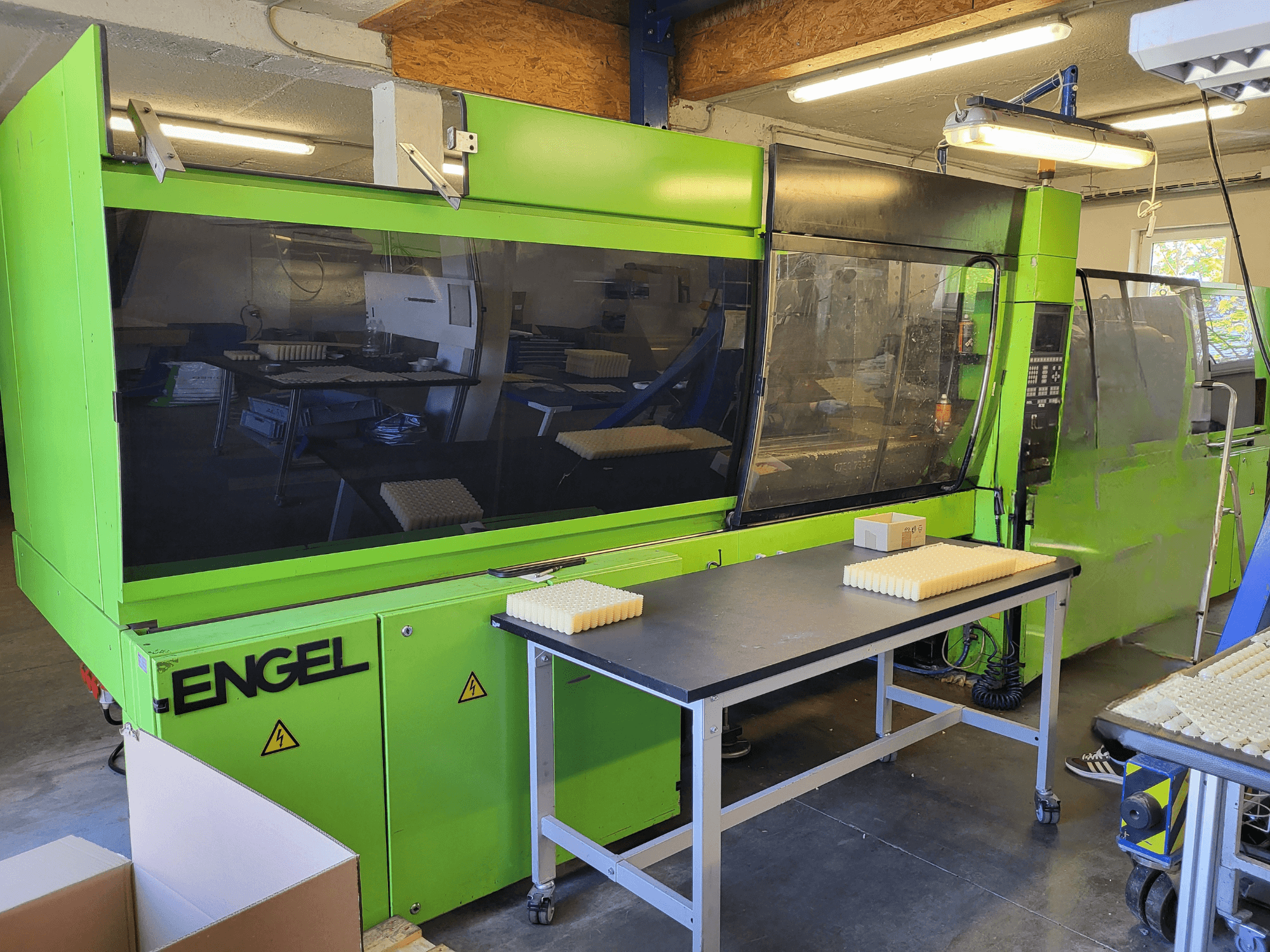 Machine de moulage par injection hydraulique Green Engel ES1800/300HL vue de face, avec des matériaux empilés sur une table de travail.