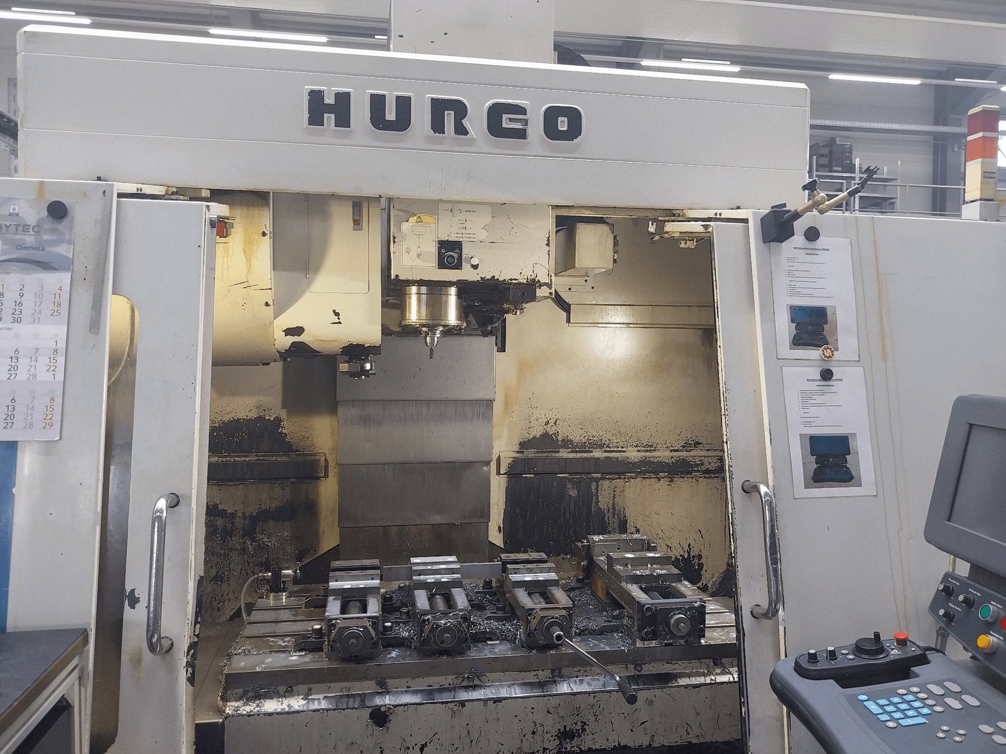 Centre d'usinage vertical Hurco VMX 42, vue de face, montrant la table de travail avec les fixations et le panneau de commande, état légèrement usé.