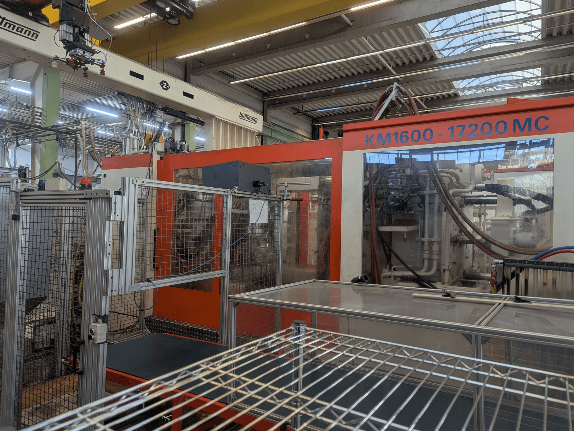 Machine de moulage par injection hydraulique Krauss Maffei KM 1600-17200MC, vue de face avec panneau de commande et conduites hydrauliques visibles.