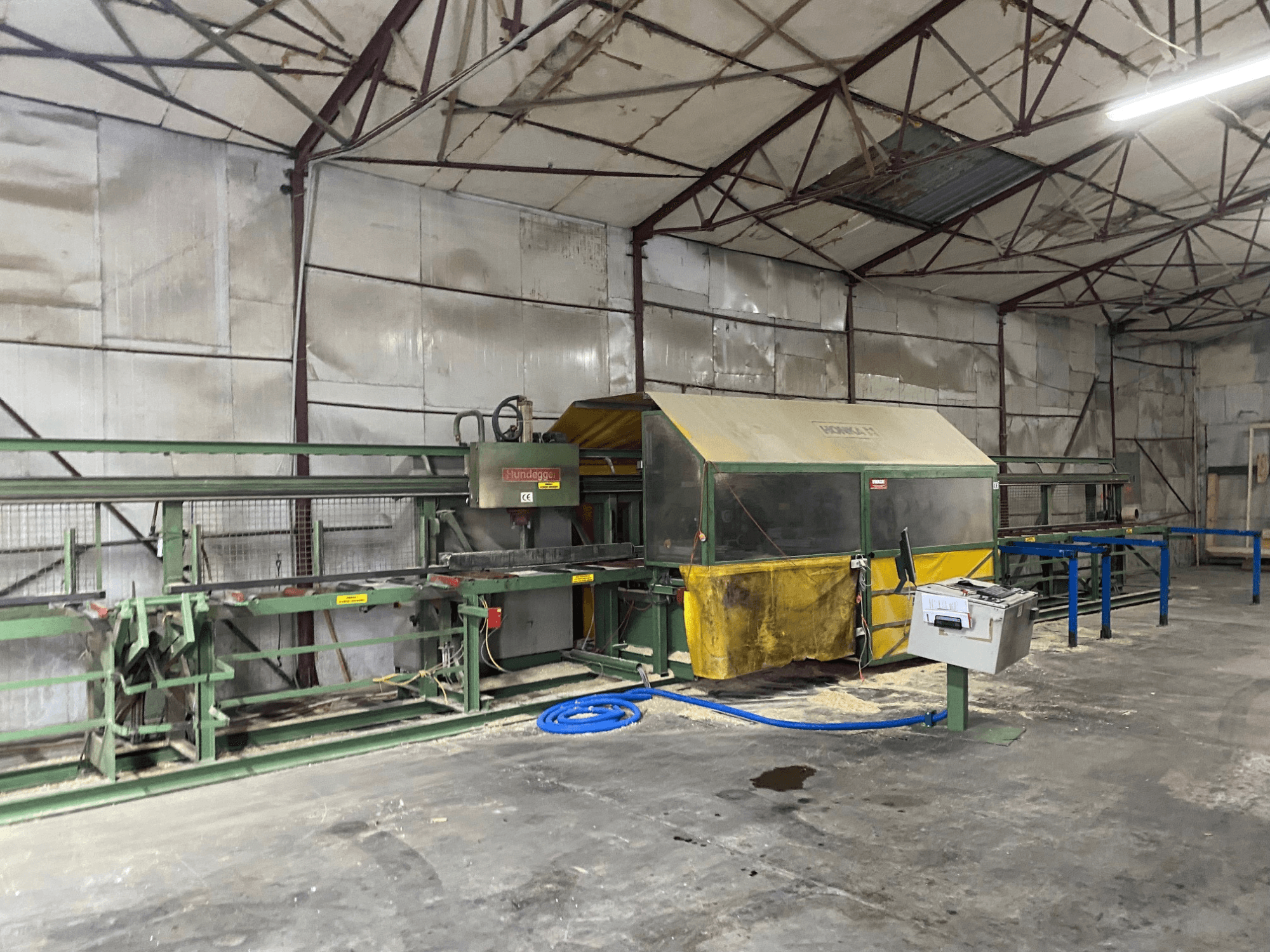 Centre d'usinage du bois CNC HUNDEGGER K1 dans un atelier, vue latérale montrant les machines, les commandes et la sciure sur le sol.