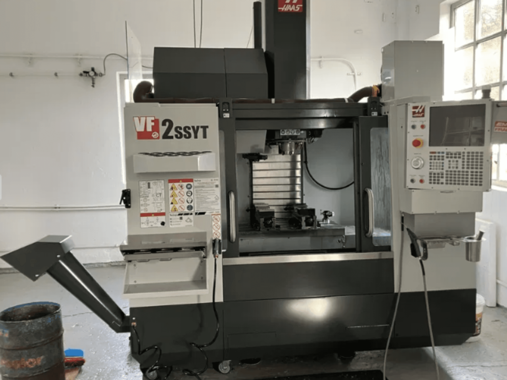 La fraiseuse CNC Haas VF-2SSYT, vue de face, comprend un panneau de commande, un porte-outil et un système d'arrosage pour l'usinage des métaux.