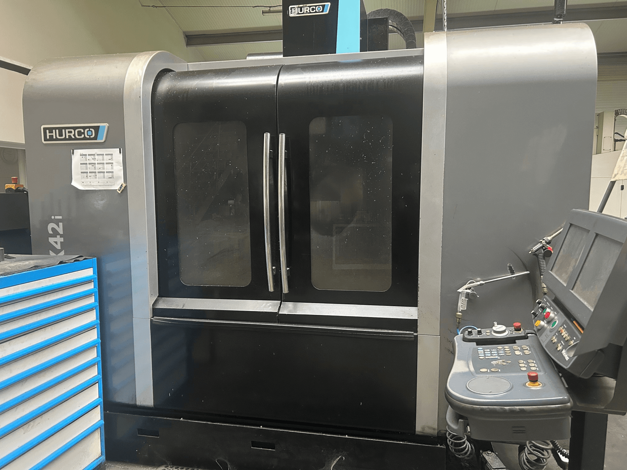 Machine CNC Hurco VMX42i, vue de face avec panneau de commande sur le côté, dotée de doubles portes et de détails techniques visibles.