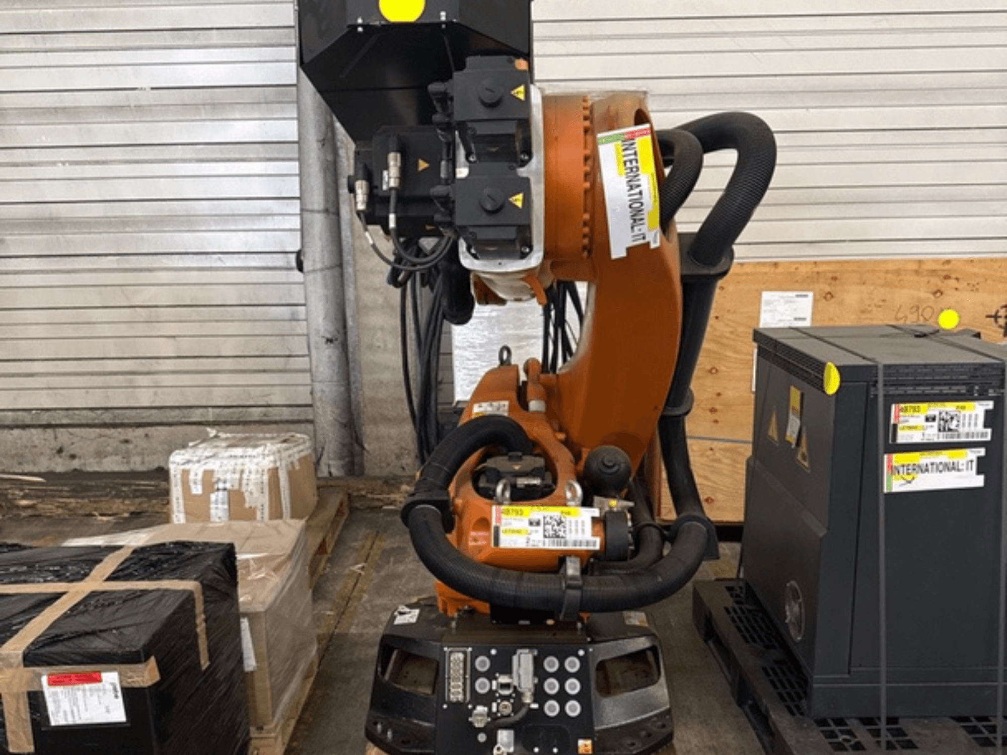 Bras de robot KUKA KR 210 R2700 supplémentaire, vu de face, présenté sur une palette à côté de colis et de matériel.