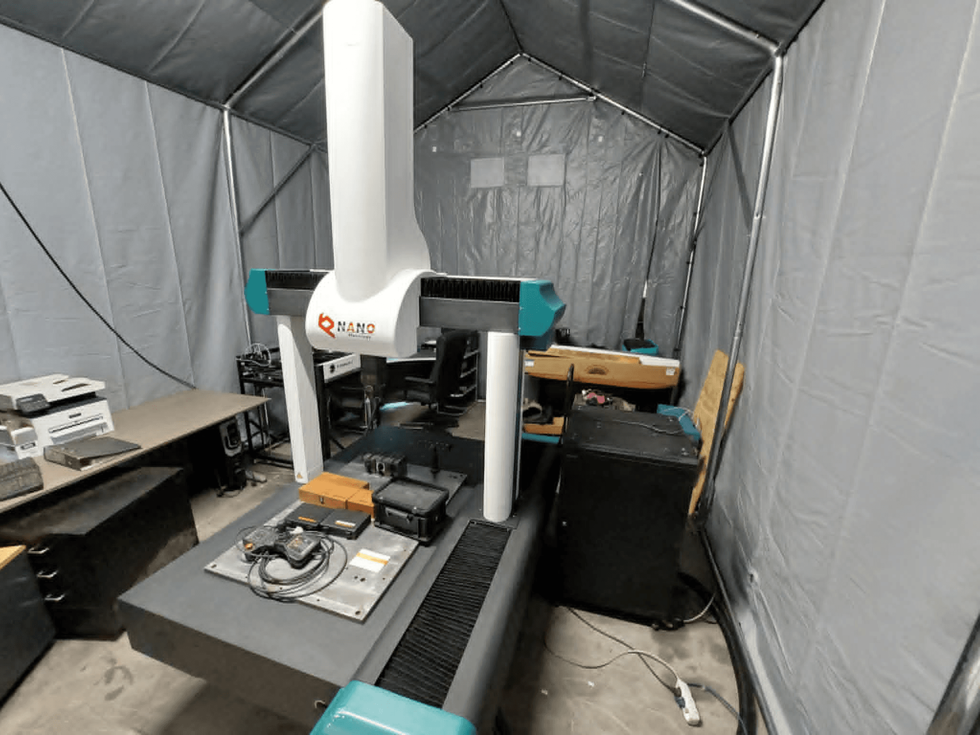 NANO METROLOGY Micr 7106 CMM dans une tente ; vue de face montrant le bras de la machine et la plate-forme de mesure avec les accessoires.