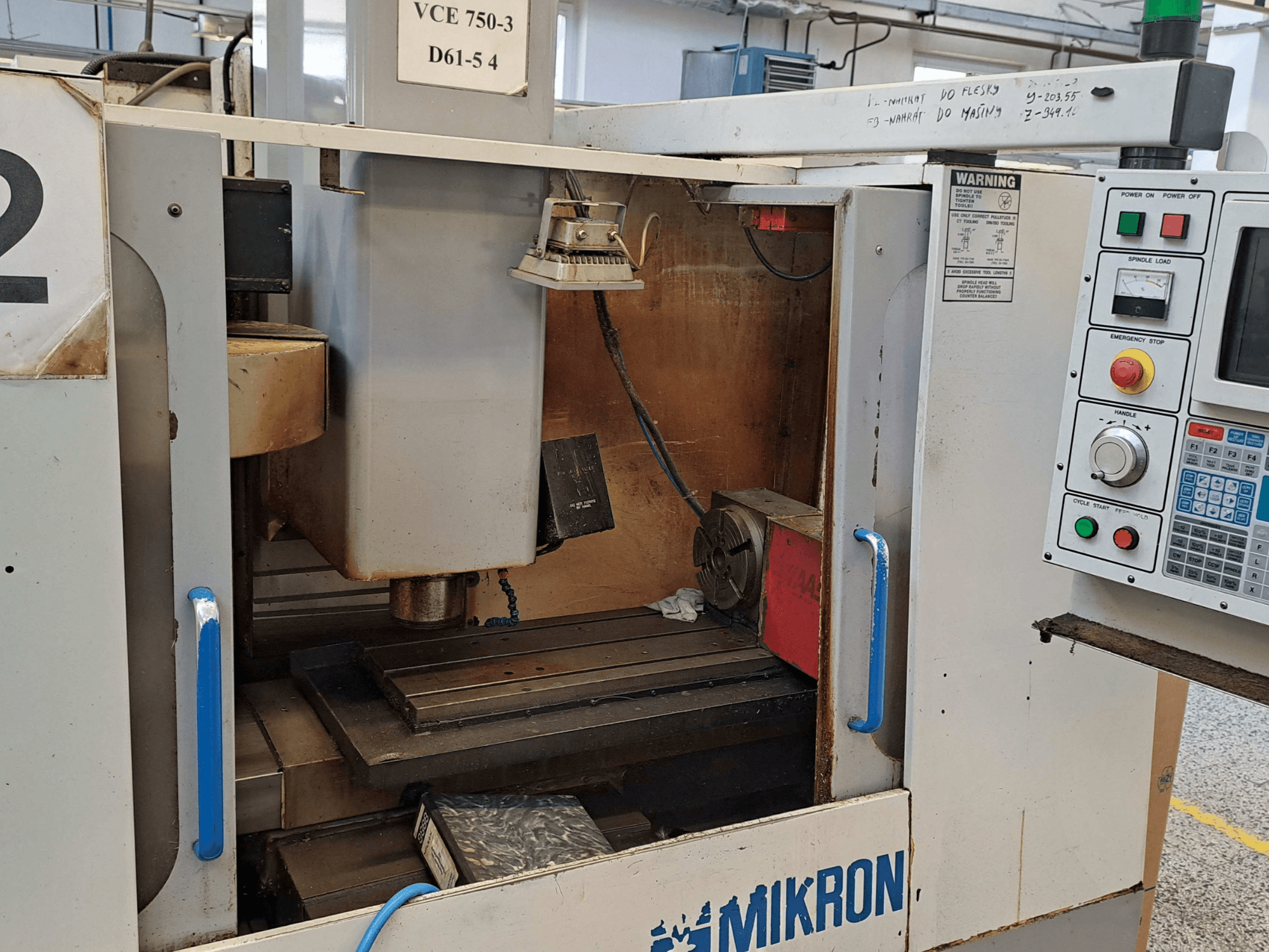 Vue de face d'une fraiseuse Mikron VCE 750-3, montrant la broche, le panneau de commande et la table de travail avec les détails techniques.