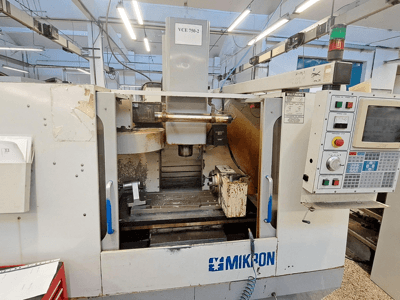 Fraiseuse CNC Mikron VCE 750-2, vue de face, avec panneau de commande et broche dans la zone d'usinage, présentant des traces d'usure et de salissure.