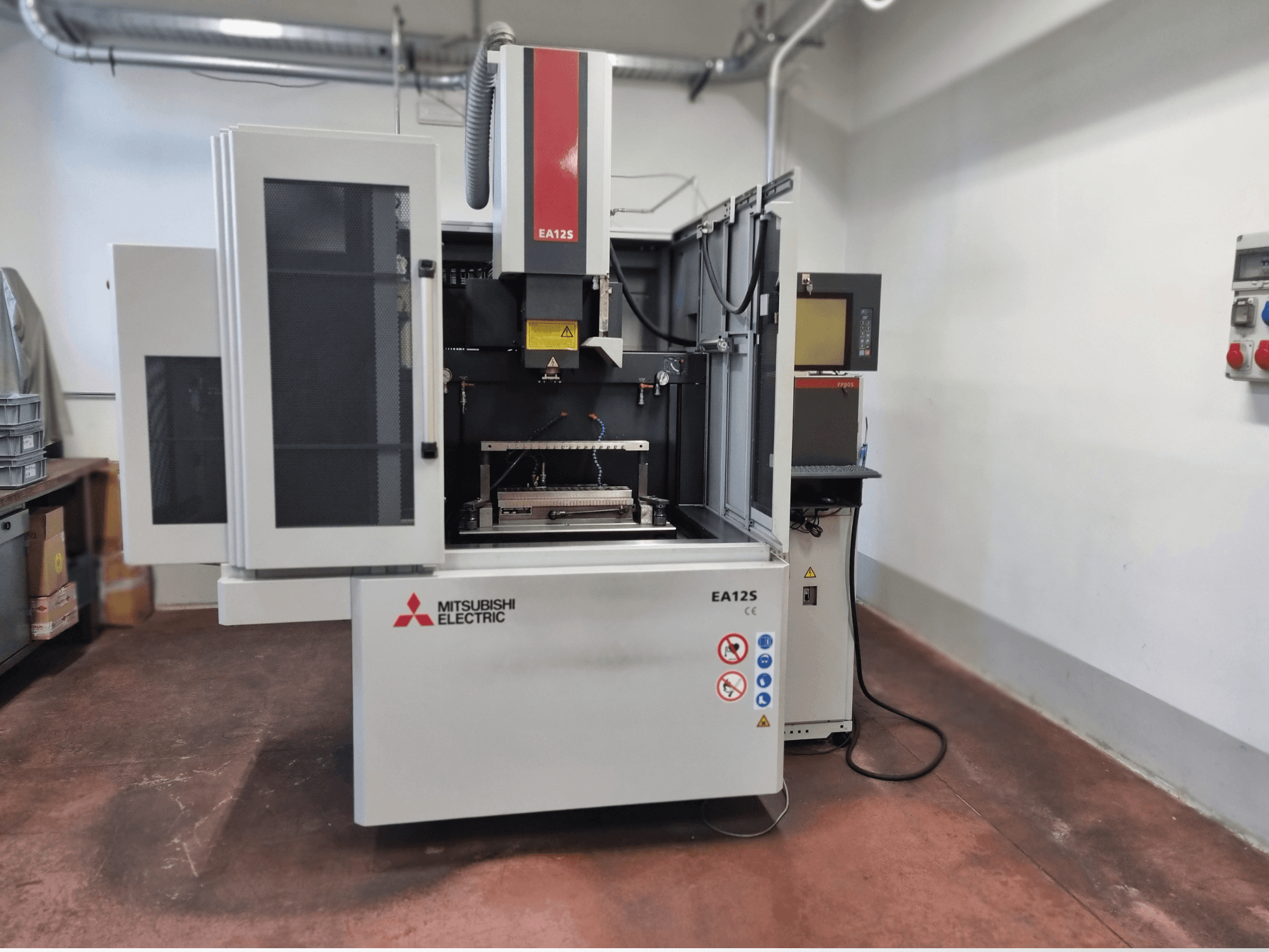 Machine de coupe de fil Mitsubishi Electric EA12S, vue de face, avec portes ouvertes, panneau de commande et étiquettes de sécurité.