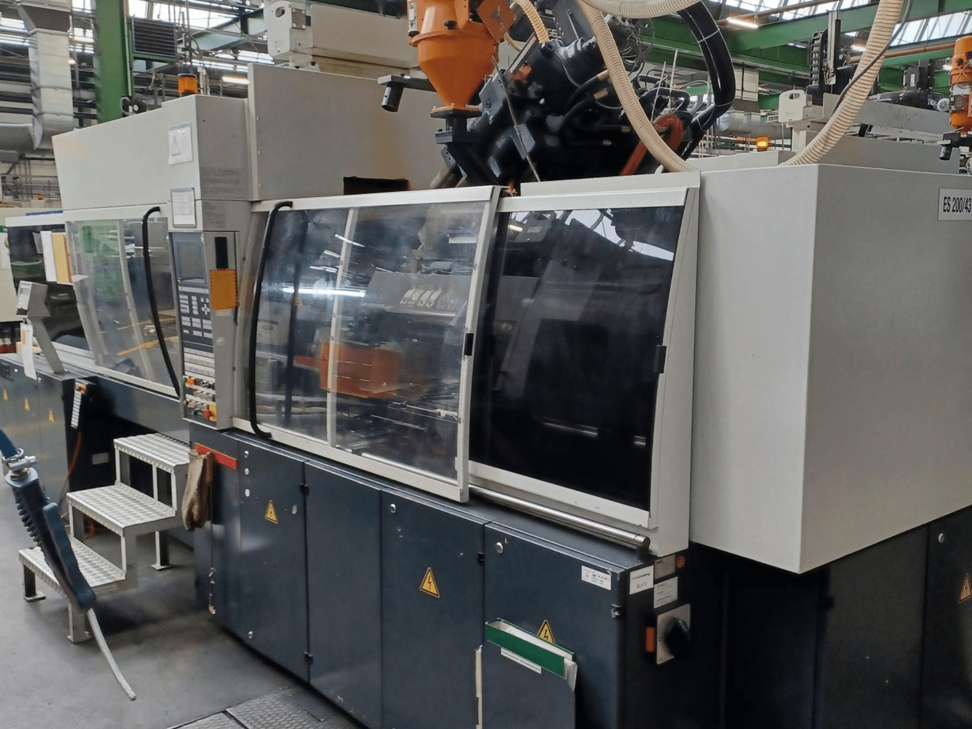 Vue de face d'une machine de moulage par injection de plastique, de marque et de modèle inconnus, comportant des portes de sécurité transparentes et un panneau de commande.