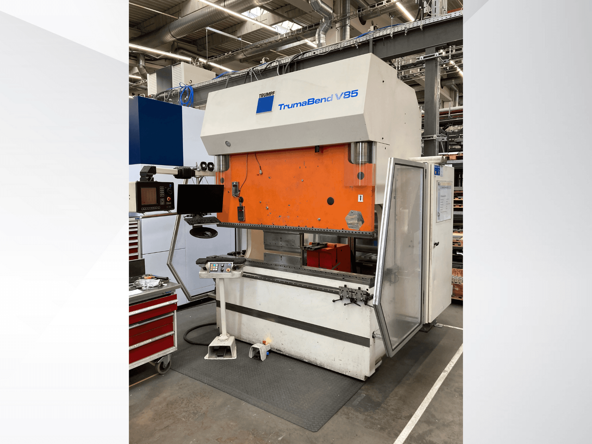 Cintreuse TruMatic V85 dans une usine, avec un panneau frontal orange, un écran de contrôle et une porte latérale ouverte, vue de côté.
