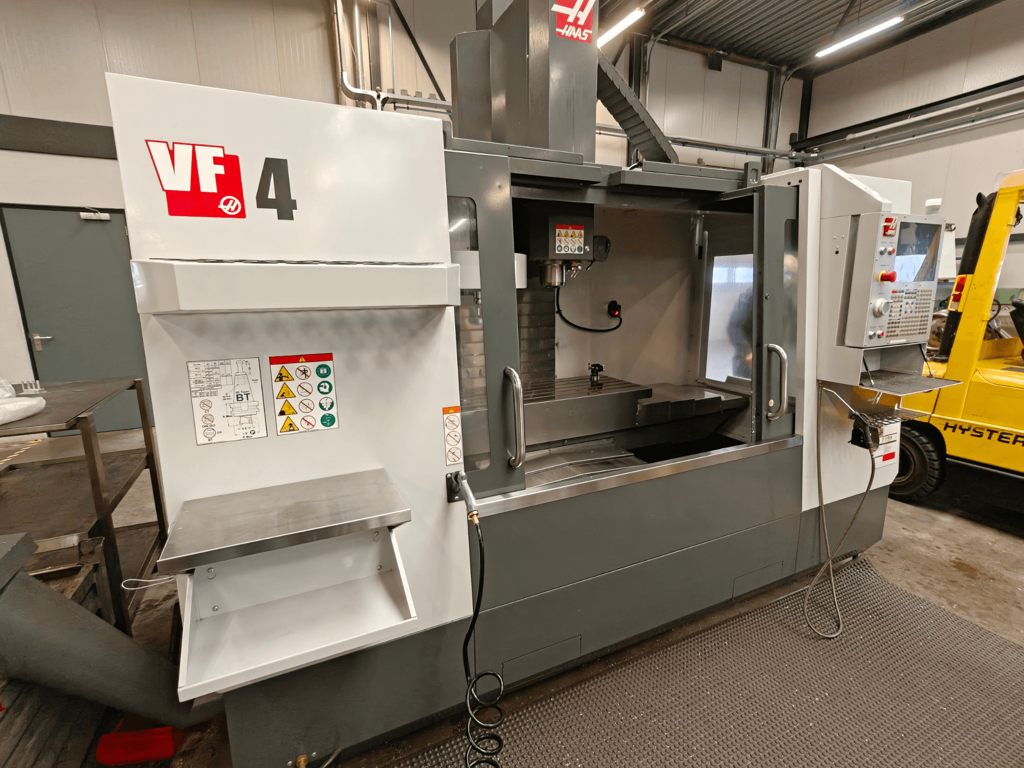 Centre d'usinage vertical HAAS VF-4, vue de face, avec panneau de commande, zone de travail et étiquettes de sécurité sur le côté.