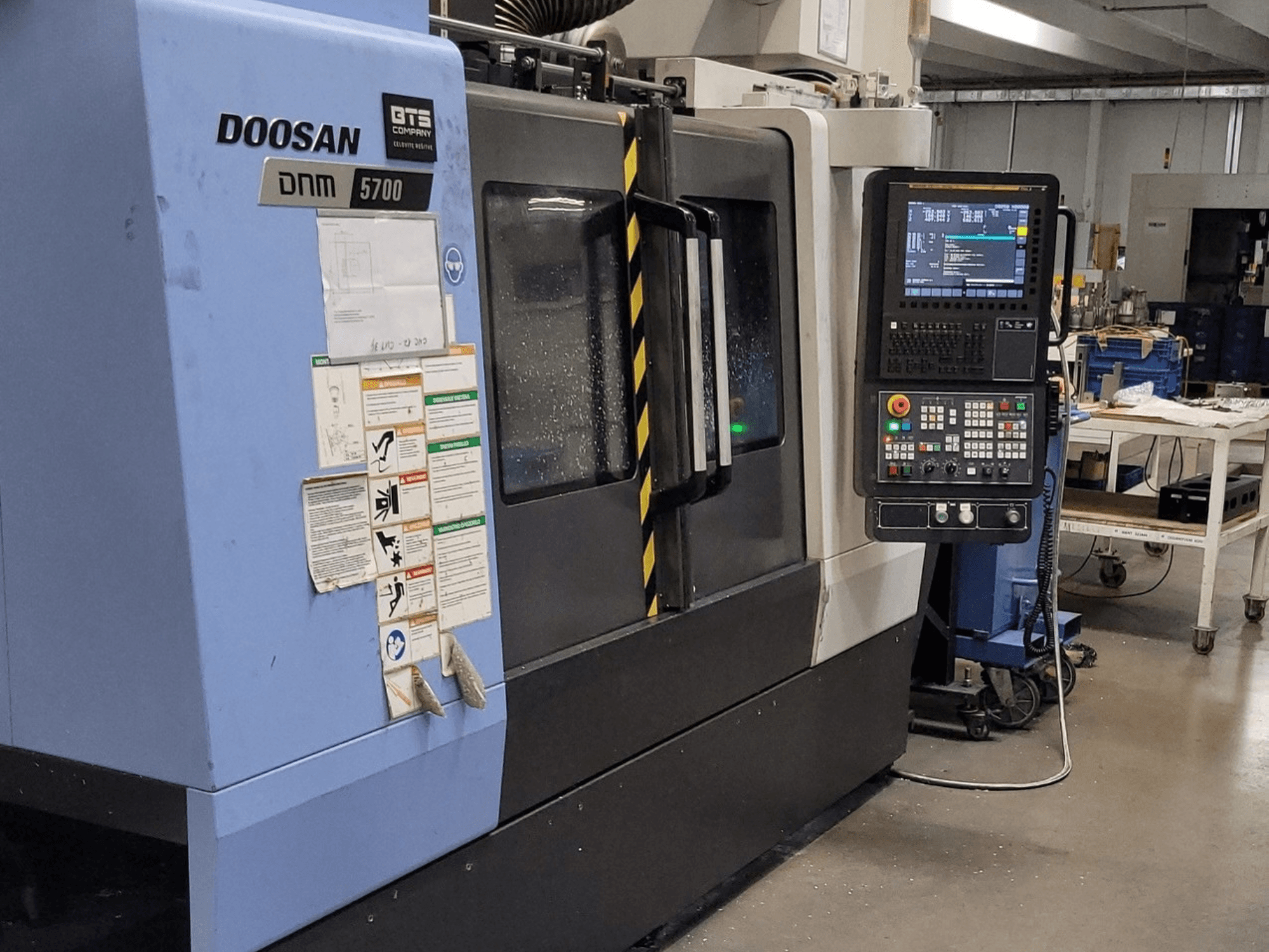Centre d'usinage vertical DOOSAN DNM 5700, vue de face, mettant en évidence le panneau de commande et les commandes opérationnelles.